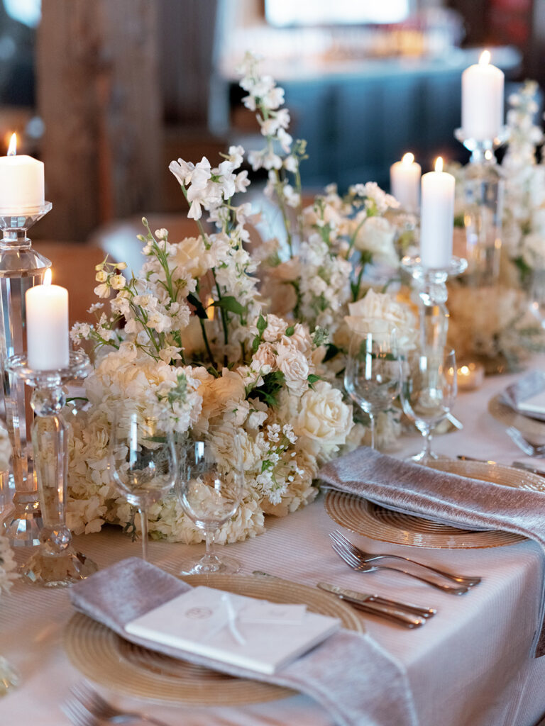 Wedding reception table decor featuring white florals, glass candle holders, custom menus at Brush Creek Ranch.