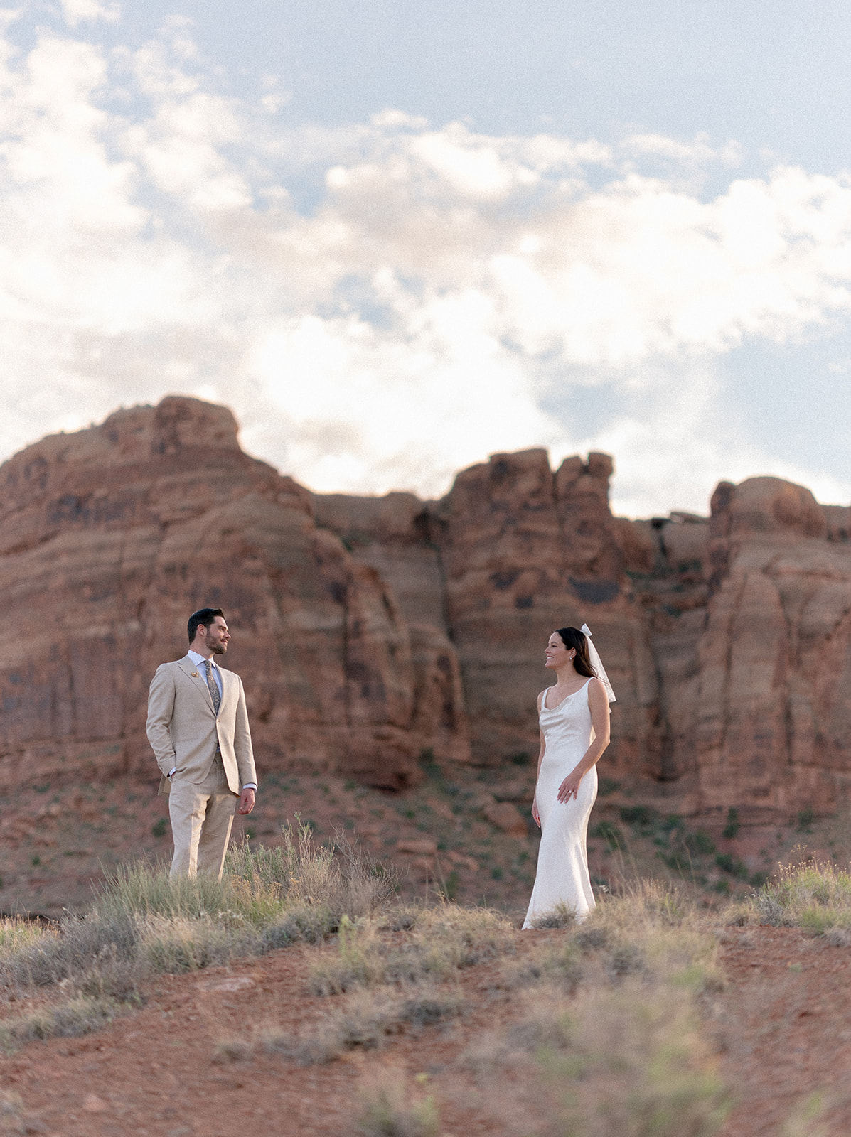 A bride and groom pose in front of red rocks in Moab, Utah.