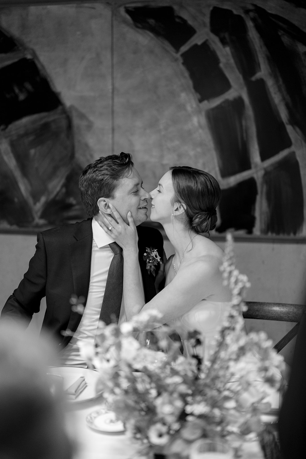 A bride holding her groom's face at their table at their Chicago indoor reception.